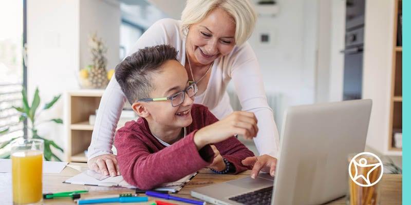 A Learning Coach and online school student smiling and engaging with a laptop